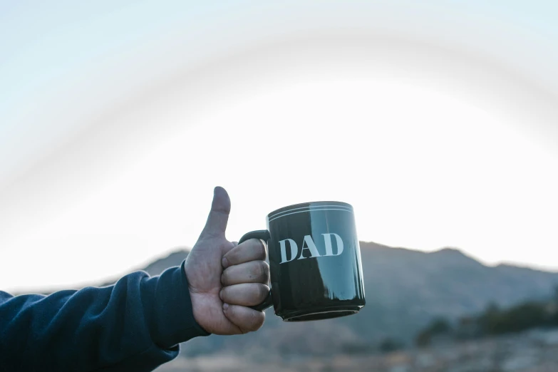 a person giving a thumbs up while holding a coffee mug, a photo, pexels contest winner, dada, i'm dad, skies, thumbnail, background image