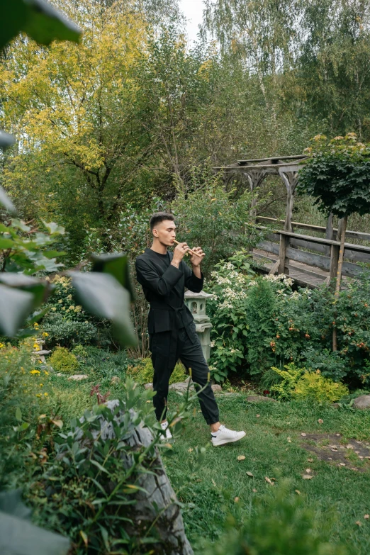 a man standing on top of a lush green field, an album cover, inspired by Ma Quan, unsplash, with a french garden, doing an elegant pose, smoking a pipe, azamat khairov