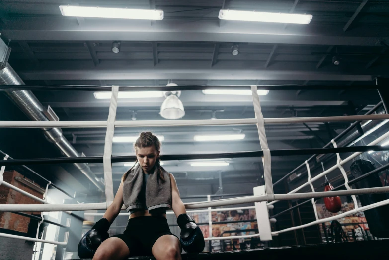 a woman sitting on the ground in a boxing ring, pexels contest winner, lachlan bailey, local gym, over it's head, manuka