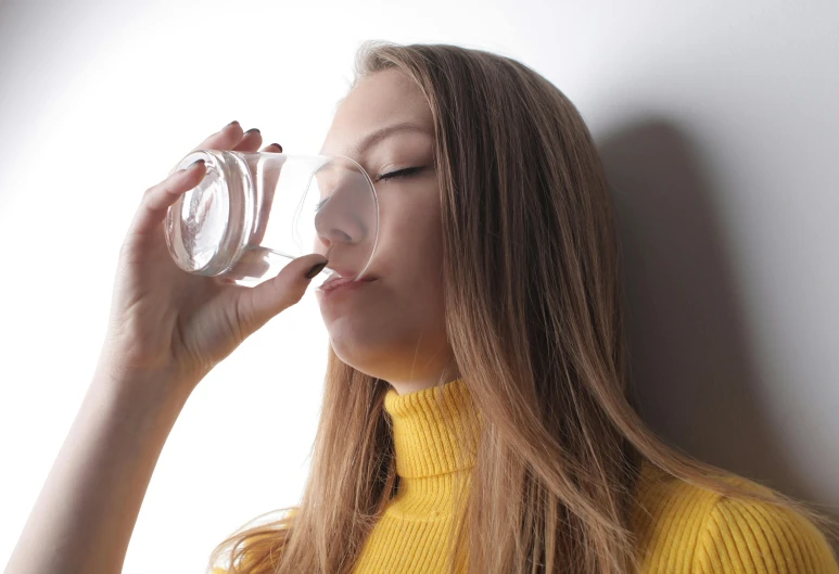 a woman in a yellow sweater drinking from a glass, a picture, trending on pexels, transhumanist hydration, wide nostrils, a blond, crystal water