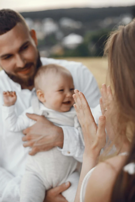 a man and woman holding a baby in a field, pexels contest winner, greeting hand on head, square, white, glossy surface