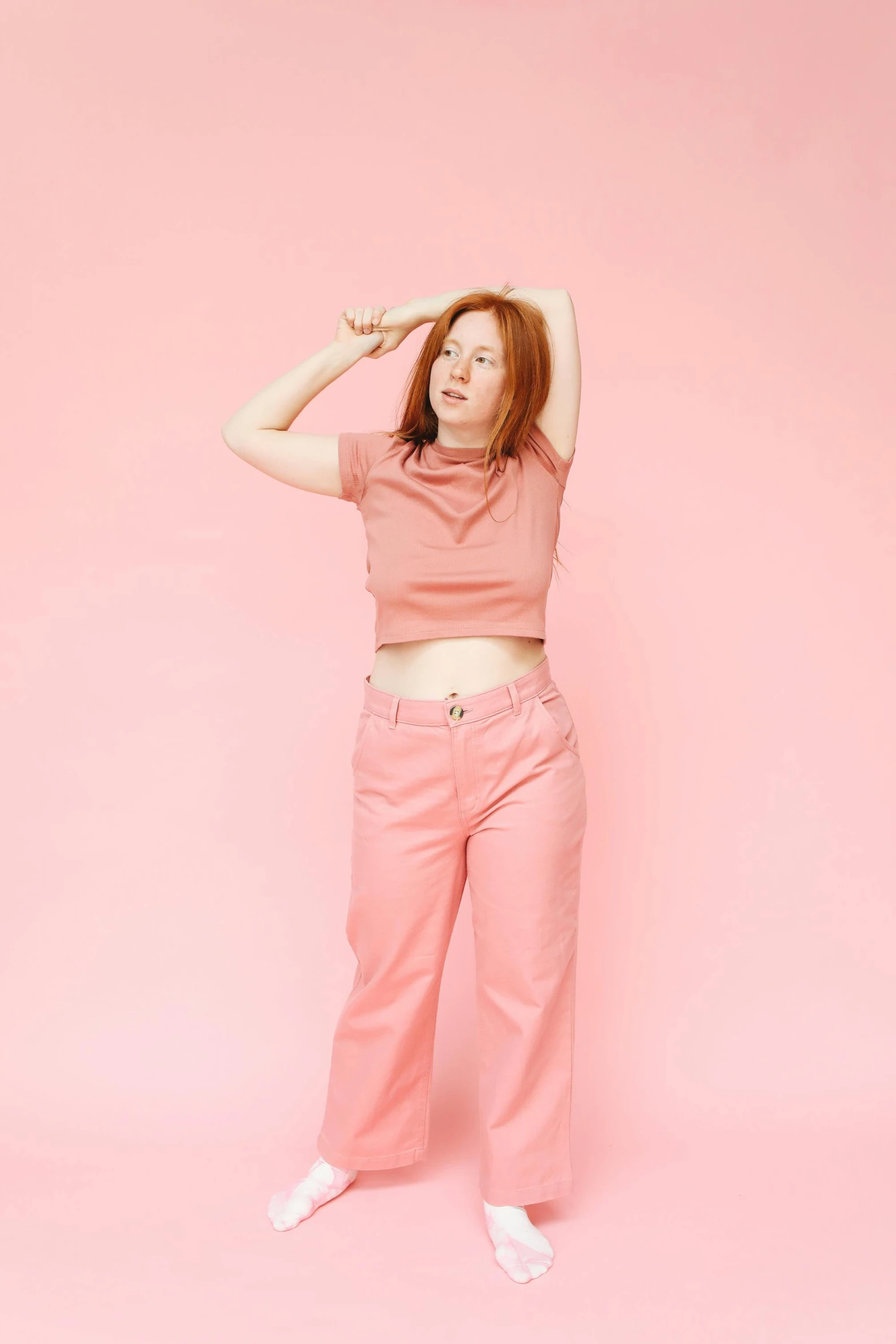 a woman standing in front of a pink background, hr ginger, wearing pants and a t-shirt, ((pink)), croptop