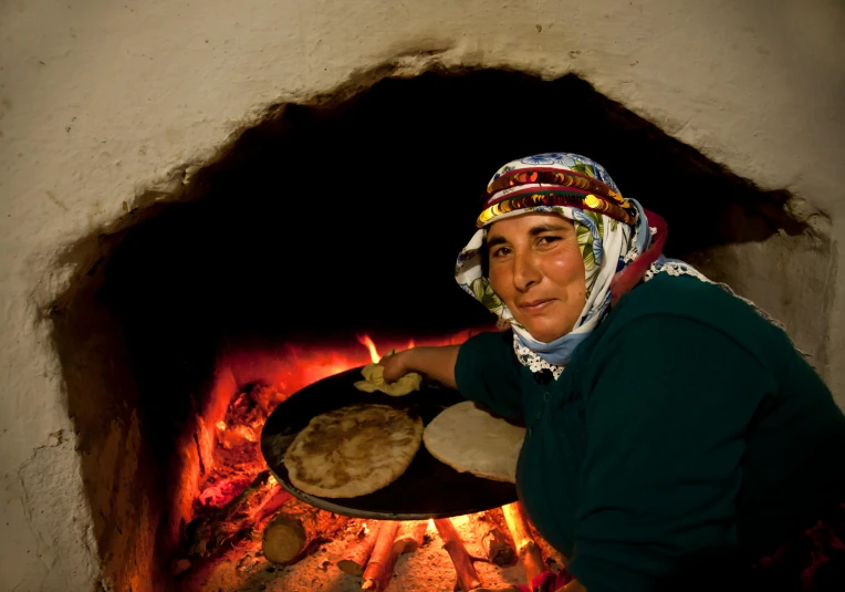 a woman holding a pan of food in front of a fire, by Julia Pishtar, hurufiyya, slide show, bakery, avatar image