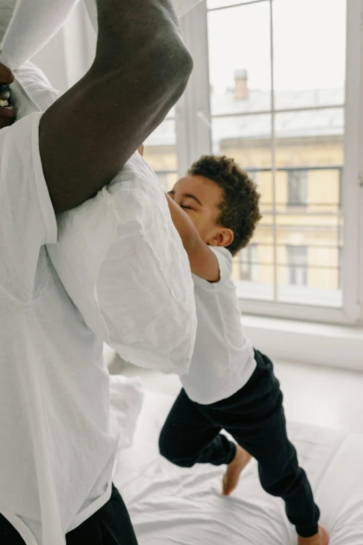 a man standing next to a little boy on top of a bed, by Nina Hamnett, pexels contest winner, white sleeves, virgil abloh, saturn devouring his son, back view. nuri iyem