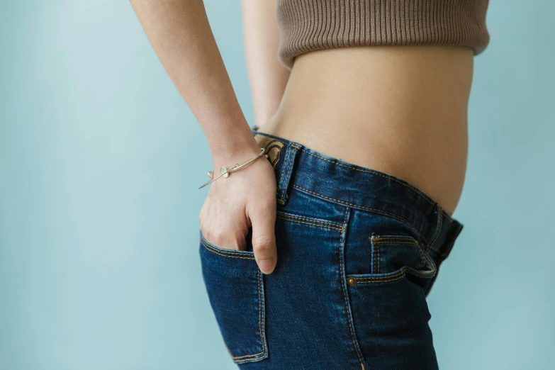 a woman with her hands in the back pocket of her jeans, by Julia Pishtar, trending on pexels, figuration libre, relaxed. blue background, belly button showing, magic belt, wearing a crop top