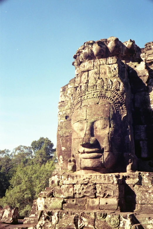 a large stone face on the side of a building, angkor thon, sun is shining, front facing the camera, view