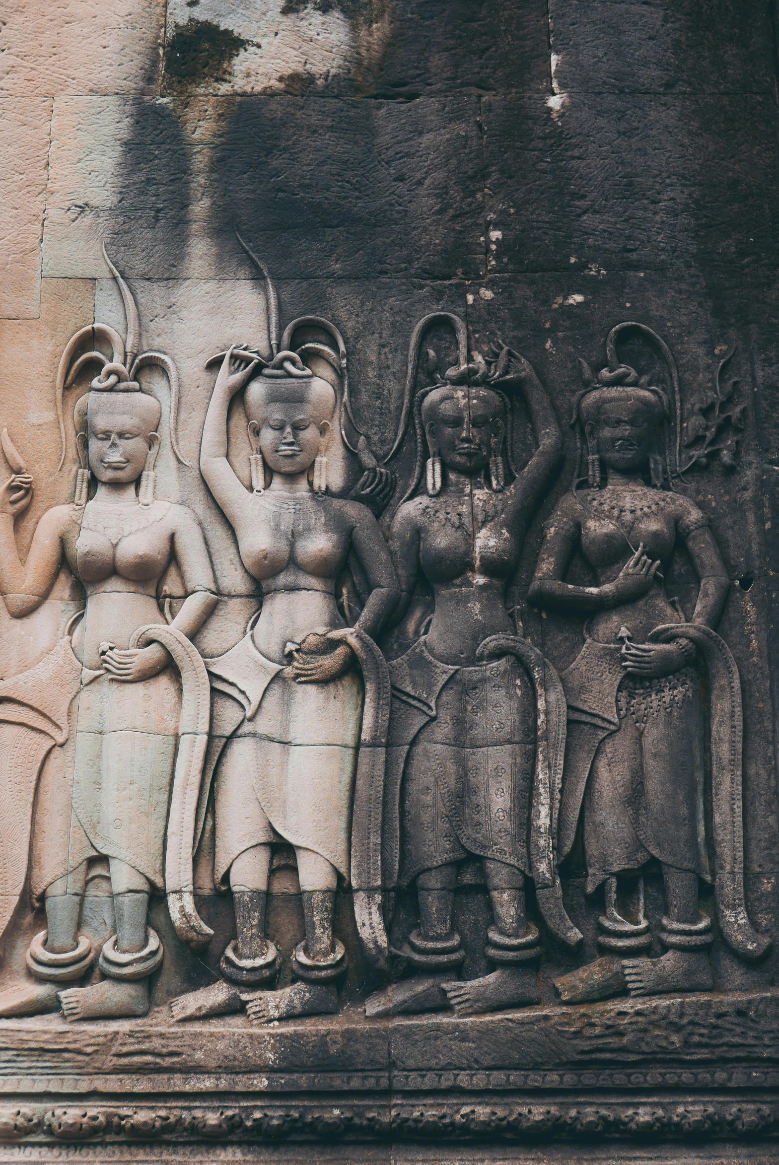 a group of statues on the side of a building, in a temple, pink and grey muted colors, three eyed goddesses, angkor