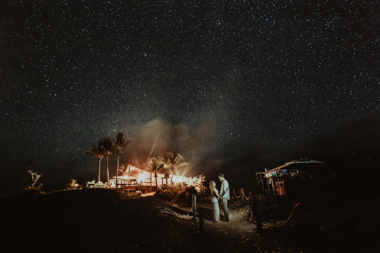 a group of people standing on top of a dirt road, by Lee Loughridge, unsplash contest winner, sitting on the beach at night, wedding, tiny stars, big island