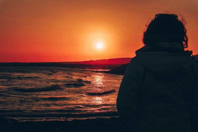 a person standing on a beach at sunset, pexels contest winner, red and orange glow, gazing off into the horizon, sunset warm spring, profile pic