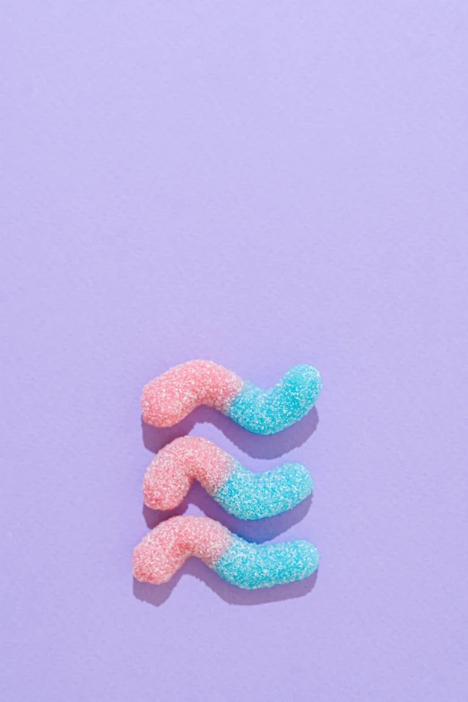 a couple of gummy worms sitting on top of a purple surface, trending on pexels, pastel blues and pinks, sugar, vine twist, 1 8
