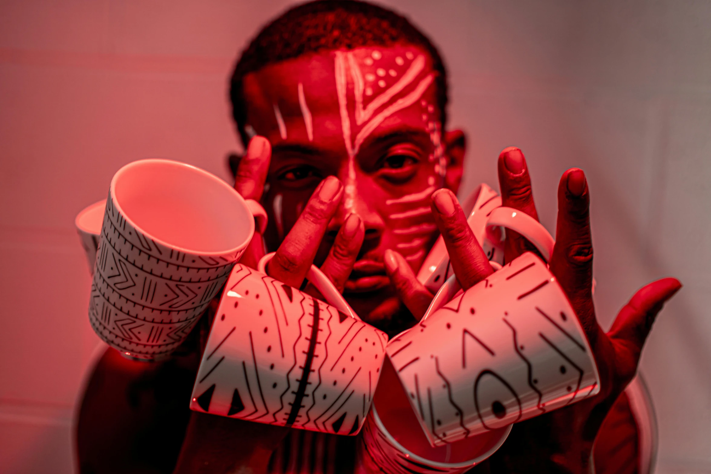 a man with red paint on his face holding a cup, an album cover, inspired by Afewerk Tekle, pexels contest winner, afrofuturism, with a white mug, patterned, underlit, coffee cups