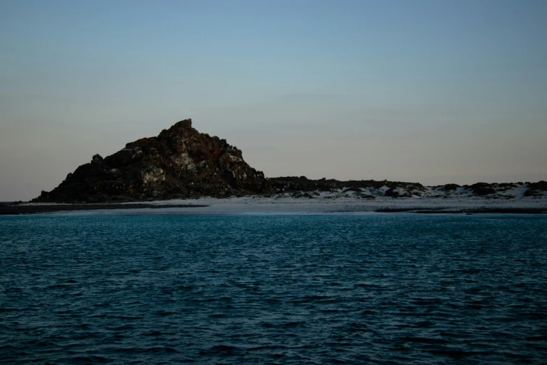 a small island in the middle of a body of water, an album cover, unsplash, hurufiyya, archipelago, early evening, in the distance is a rocky hill, blue sand