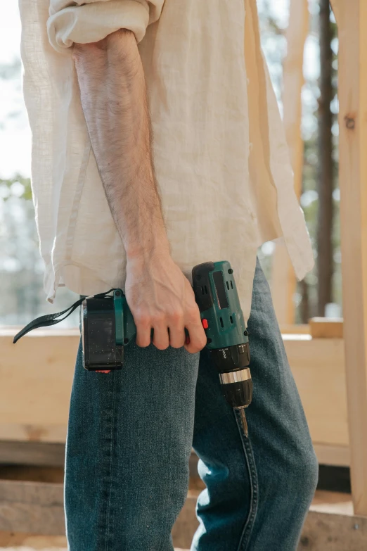 a close up of a person holding a drill, by Ben Zoeller, wearing pants and a t-shirt, passive house, double denim, lightweight