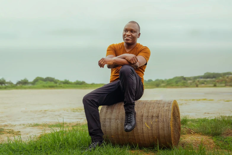 a man sitting on top of a wooden barrel, an album cover, pexels contest winner, david uzochukwu, on a riverbank, confident pose, he is about 20 years old | short