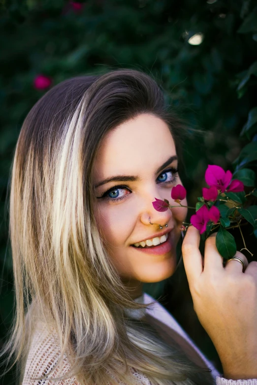 a woman holding a flower in front of her face, inspired by Elsa Bleda, unsplash, blonde hair blue eyes, smiling into the camera, half - length photo, 5 0 0 px models