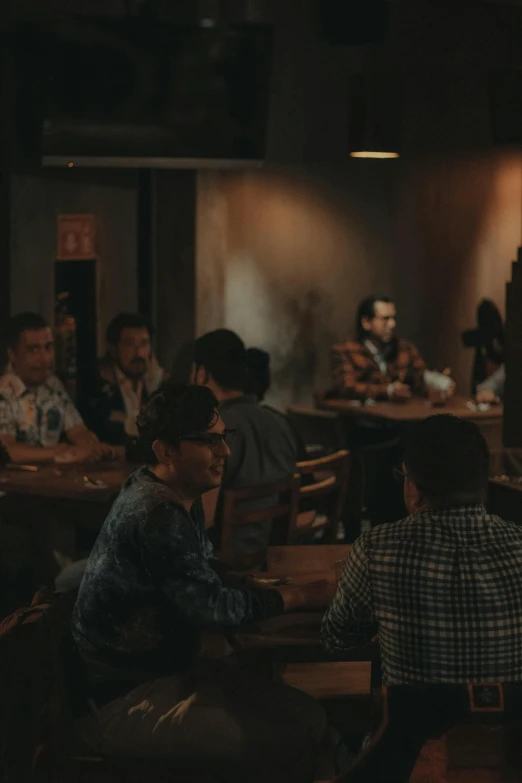 a group of people sitting at tables in a restaurant, by Alejandro Obregón, trending on unsplash, serial art, vhs footage of a movie set, mid-shot of a hunky, cinematic. by leng jun, film still promotional image