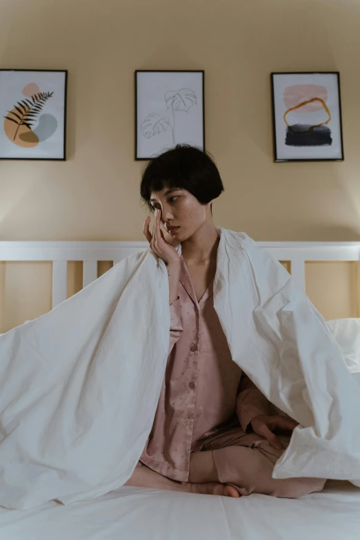 a woman sitting on top of a bed under a blanket, inspired by Yu Zhiding, pexels contest winner, visual art, wearing lab coat and a blouse, set on singaporean aesthetic, concerned, at home