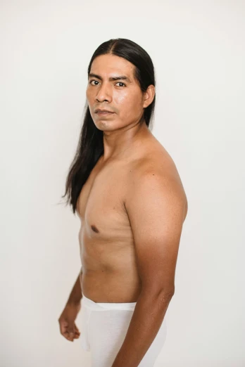 a man with no shirt standing in front of a white wall, an album cover, inspired by Jorge Jacinto, wearing a native american choker, ignant, meet the actor behind the scenes, bao phan
