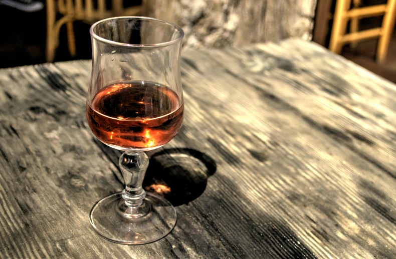 a glass of wine sitting on top of a wooden table, pexels contest winner, renaissance, brown and pink color scheme, rum, jerez, wandering