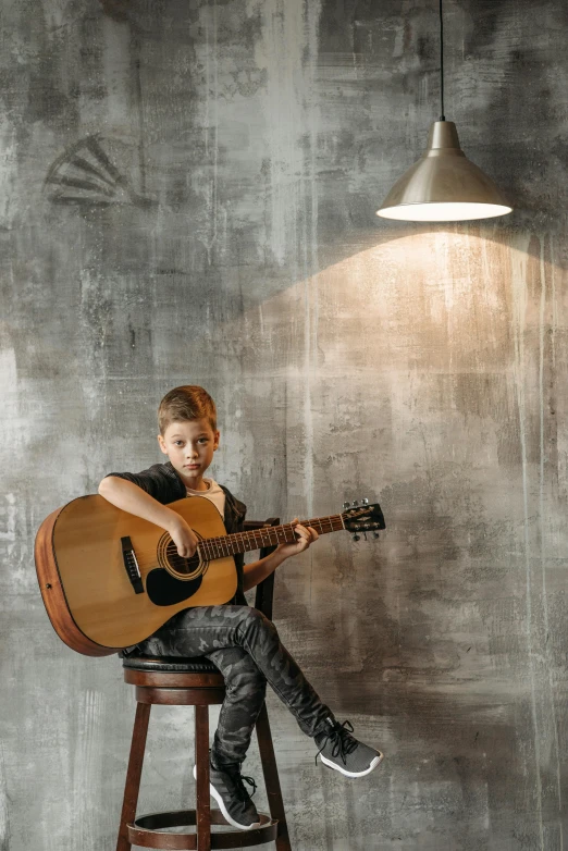 a woman sitting on a stool playing a guitar, light over boy, grey backdrop, teenager hangout spot, trending on