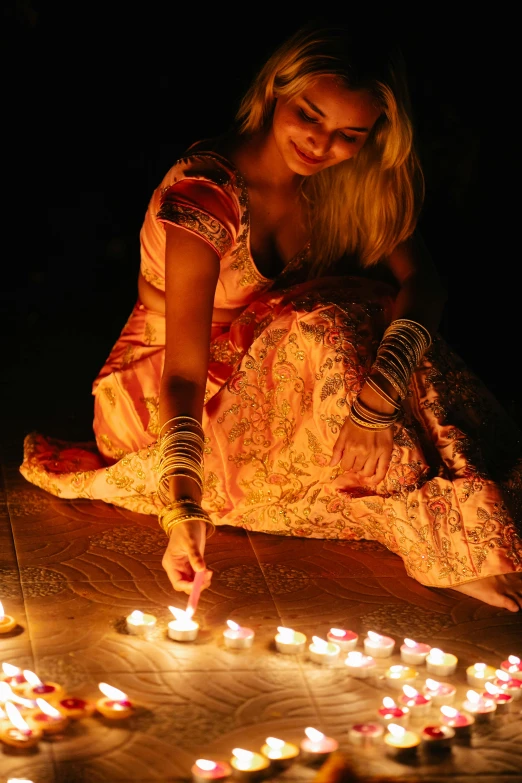 a woman sitting on the ground lighting candles, dancefloor kismet, glowing ceremonial markings, very vibrant, sharandula