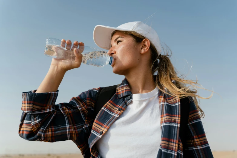 a woman drinking water out of a plastic bottle, pexels contest winner, wearing baseball cap, avatar image, drought, upper body image