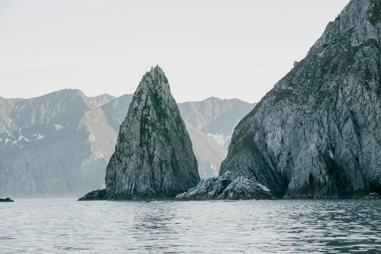 a couple of large rocks sitting on top of a body of water, by Alexander Johnston, unsplash contest winner, bjarke ingels, new zealand, asymmetrical spires, sharp cliffs