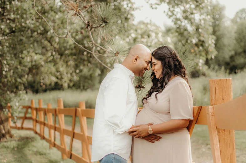 a pregnant couple standing next to a wooden fence, by Everett Warner, pexels contest winner, symbolism, background image, indian, close up half body shot, thumbnail