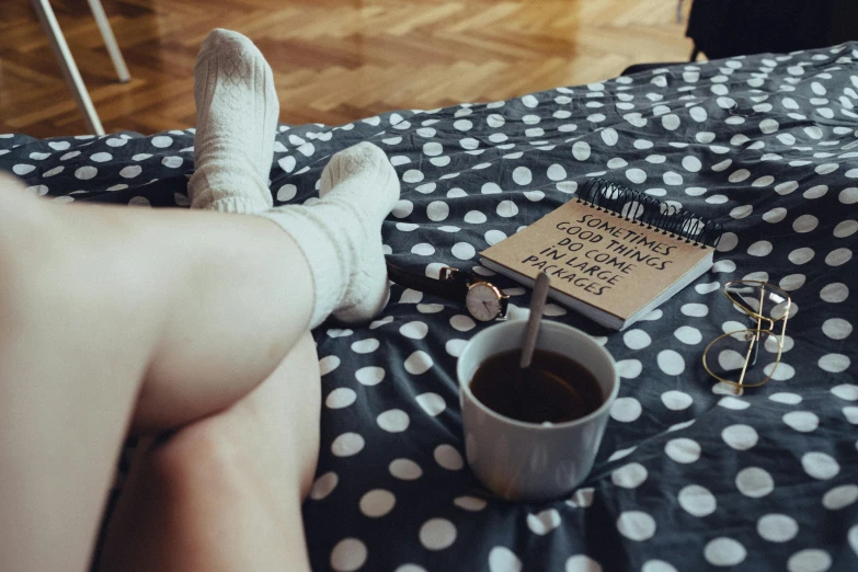 a person sitting on a bed with a book and a cup of coffee, inspired by Elsa Bleda, trending on pexels, antipodeans, thigh high socks, drinking cough syrup, polka dot, lying on an empty