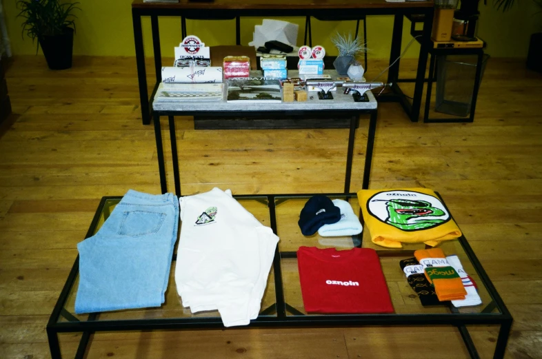 a table topped with assorted items on top of a wooden floor, happening, outlive streetwear collection, gallery display photograph, gifts, a green