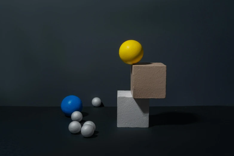 a yellow ball sitting on top of a block next to blue and white balls, an abstract sculpture, inspired by Bauhaus, unsplash, behance lemanoosh, dough sculpture, videogame still, cube