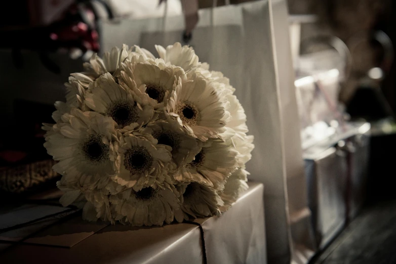 a bouquet of white flowers sitting on top of a counter, by Lucia Peka, pexels contest winner, beige and dark atmosphere, gifts, head made of giant daisies, shot on sony a 7