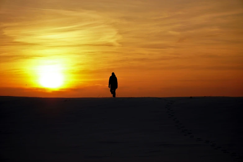 a person walking across a snow covered field at sunset, pexels contest winner, pilgrimage, silhouette :7, looking sad, sunset on mars