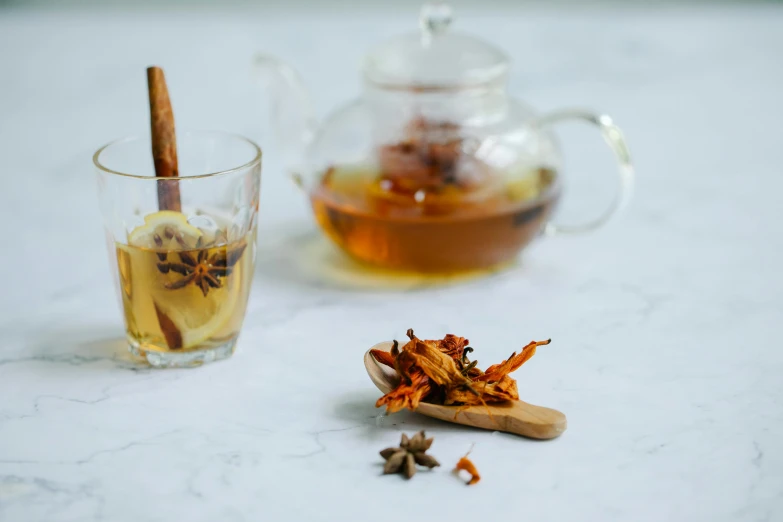 a cup of tea and a teapot on a table, a still life, by Arabella Rankin, trending on pexels, spices, trapped in tall iced tea glass, dried petals, bespoke