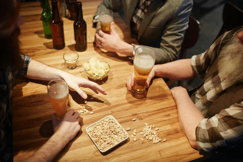 a group of people sitting around a wooden table, by Matthias Stom, pexels, beer being drank and spilled, straya, snacks, nighthawks