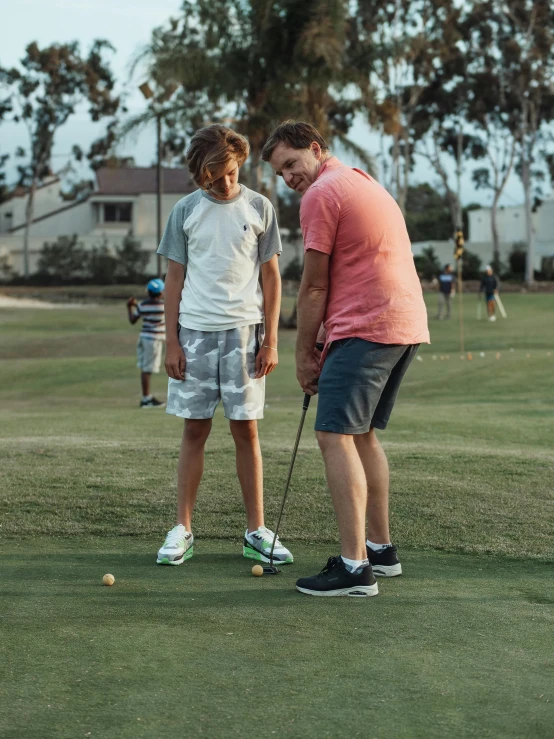 a man teaching a boy how to put a golf ball, a picture, pexels contest winner, happening, boy shorts, low quality photo, thumbnail, oceanside