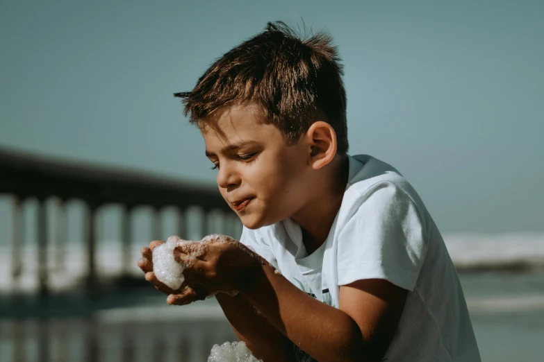 a young boy sitting on top of a sandy beach, pexels contest winner, covered in white flour, side profile shot, avatar image, holding a white duck
