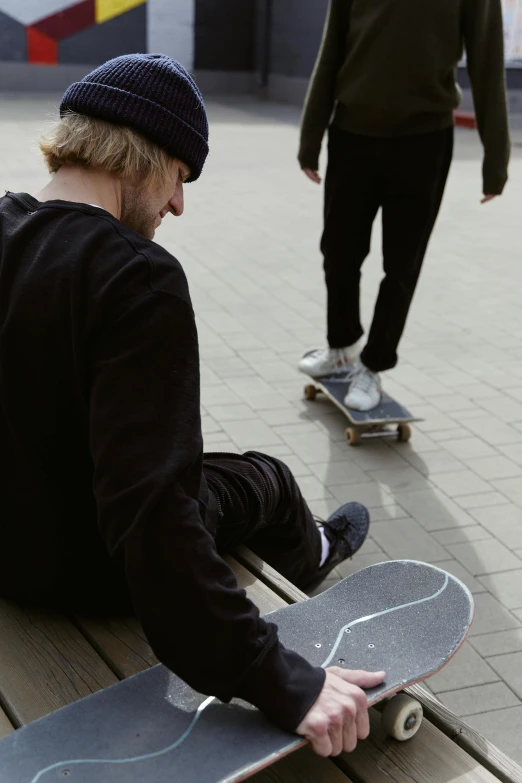 a man sitting on a bench with a skateboard, a picture, by Jaakko Mattila, unsplash, medium shot of two characters, low quality footage, dynamic skating, a high angle shot