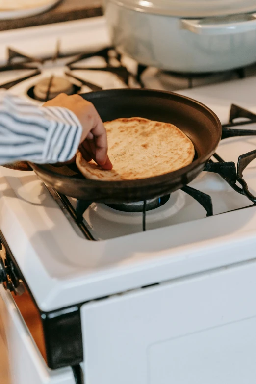 a person cooking food in a frying pan on a stove, by Carey Morris, flat pancake head, fan favorite, fully covered, at home