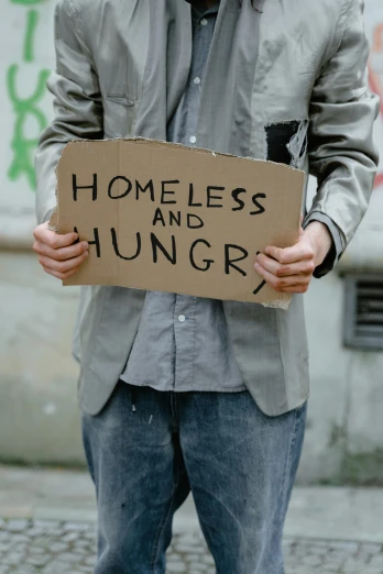 a man holding a sign that says homeless and hungry, an album cover, shutterstock, sustainability, teenager, 2 0 2 0 fashion, battered
