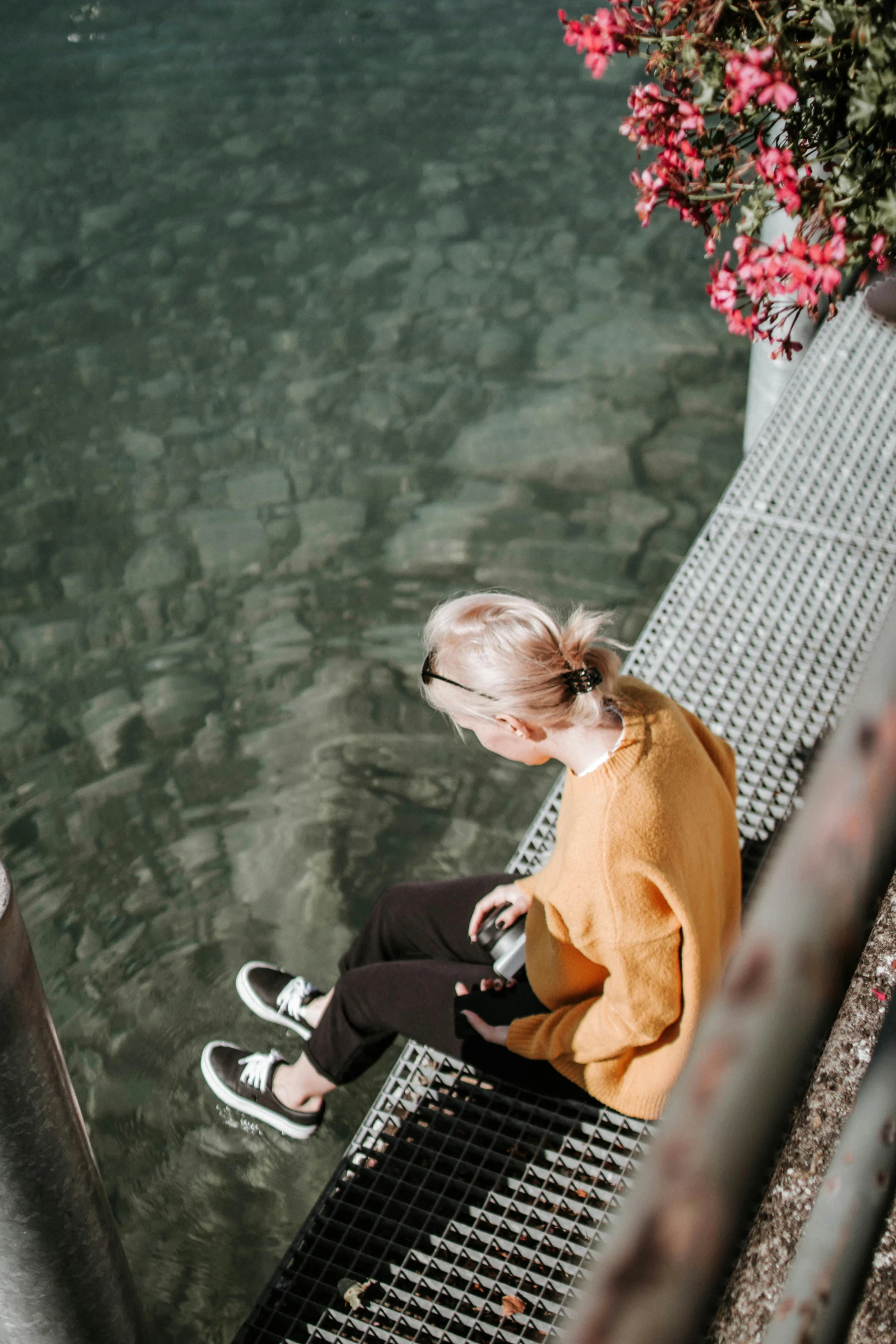 a woman sitting on a bench next to a body of water, by Niko Henrichon, trending on unsplash, yellow hair, looking down from above, casual streetwear, switzerland