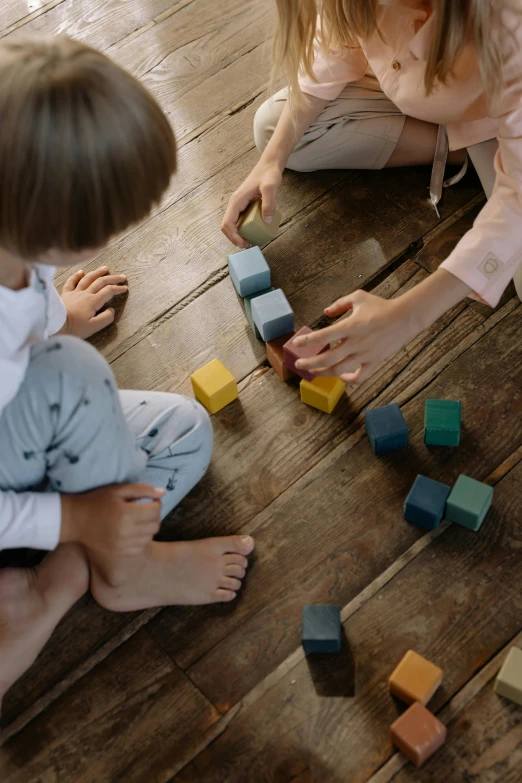 two children playing with wooden blocks on the floor, by Sebastian Vrancx, pexels, square shapes, color footage, woman, grey