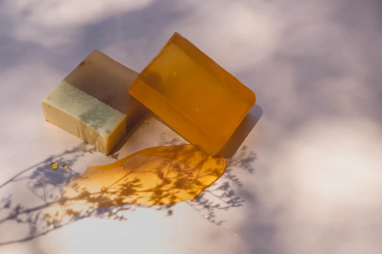 a couple of soap bars sitting on top of a snow covered ground, by Emma Andijewska, unsplash, renaissance, liquid translucent amber, with seaweed, square shapes, sun lit