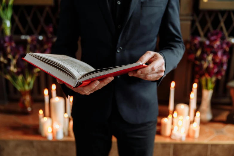 a man in a suit holding an open book, an album cover, by Julia Pishtar, pexels contest winner, romanticism, candles, 15081959 21121991 01012000 4k, funeral, mid body shot