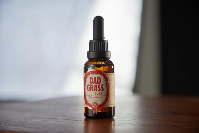 a bottle of liquid sitting on top of a wooden table, a picture, patches of red grass, dad energy, shaven stubble, on textured base; store website