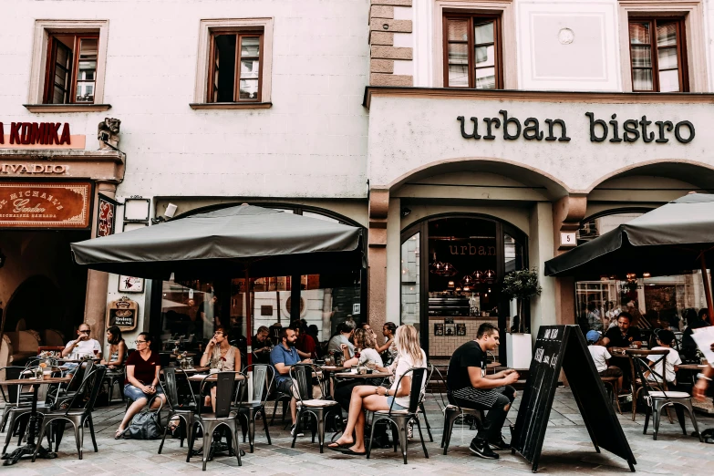 a group of people sitting at tables outside of a restaurant, by Julia Pishtar, unsplash contest winner, urban art, “ iron bark, a quaint, where a large