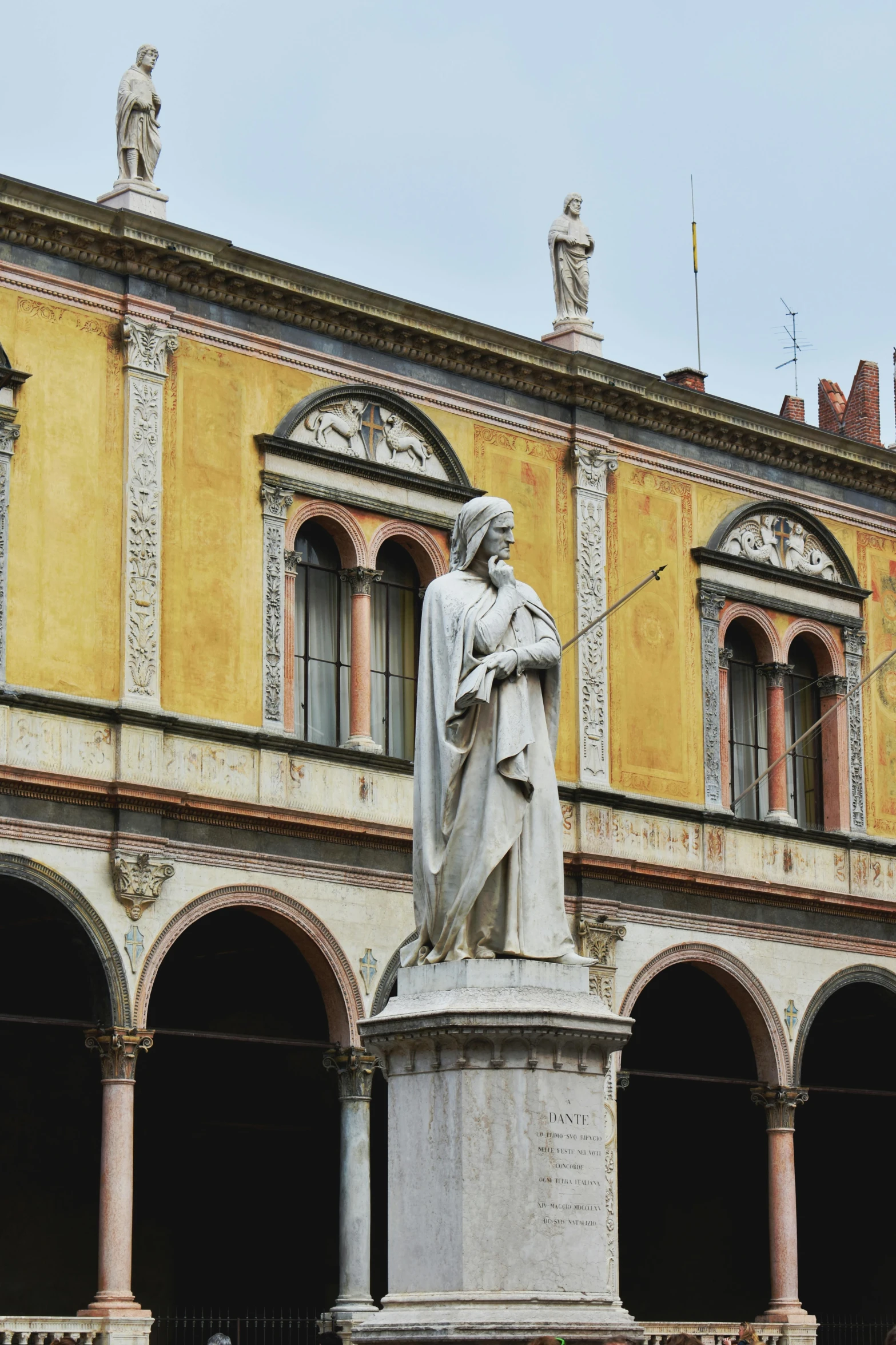 a statue of a man standing in front of a building, a statue, inspired by Giovanni Bernardino Mazzolini, wearing a flowing cloak, market square, holding a sword on her shoulder, with yellow cloths