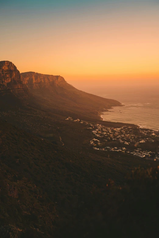 a view of the ocean from the top of a mountain, in a golden sunset sky, south african coast, “ aerial view of a mountain, city sunset