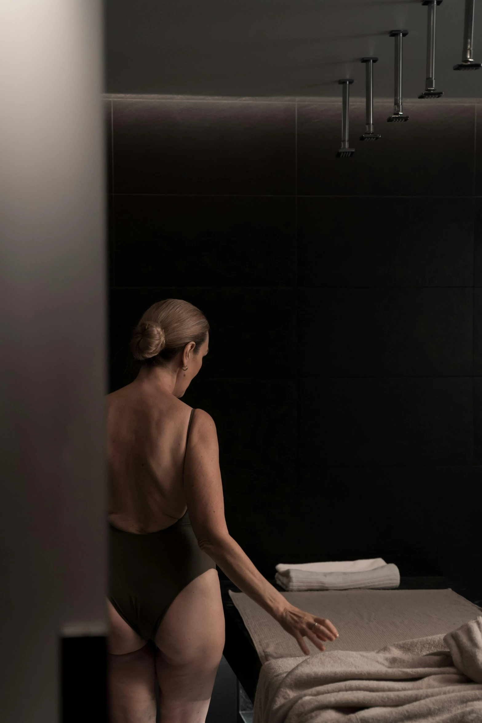 a woman in a bathing suit standing next to a bed, inspired by Nan Goldin, unsplash, renaissance, showers, 3 / 4 view from back, on black background, spa