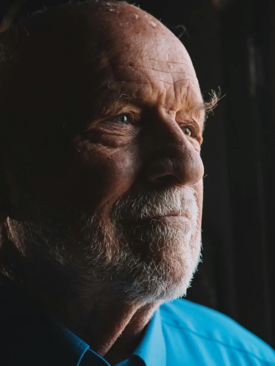 a close up of a person wearing a blue shirt, an old man, window light, profile image, grumpy [ old ]